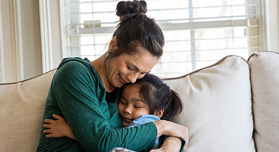 A woman hugs her young daughter and smiles