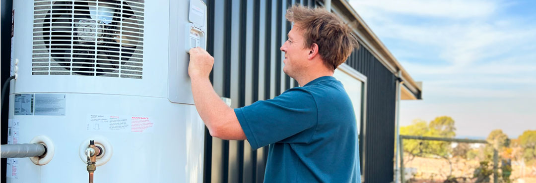 A man checks the settings on a heat pump outside his home