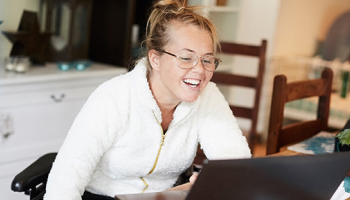 A woman smiles while looking at her laptop
