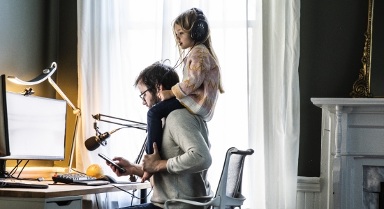 A parent working from home with their child on their shoulders