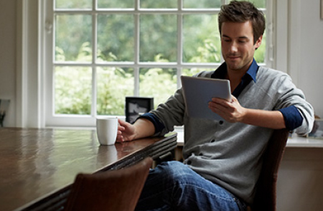 man at a desk with a cup of coffee reading a tablet