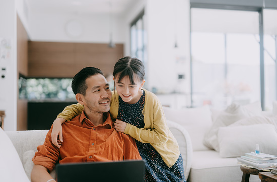 A dad and his young daughter looking at a laptop screen at home.