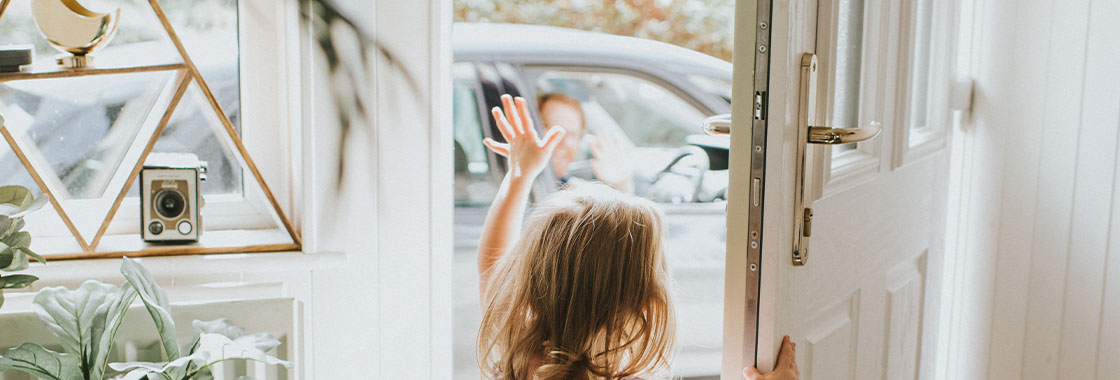 Young girl waves through the front door at a driver who waves back from inside their vehicle in the driveway.