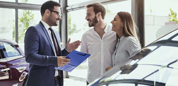 A dealer speaking to a man and a woman at a dealership, all smiling