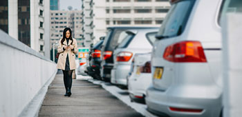 A woman walking behind a row of parked cars looking at her phone.
