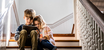 Two kids sitting on a set of stairs while looking at a tablet