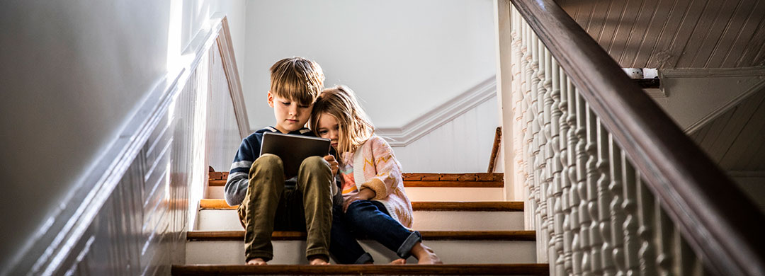 Two kids sitting on a set of stairs while looking at a tablet