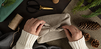 A present wrapped in a linen napkin next to a ball of string and a pine cone. 