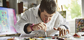 Mid adult man with down syndrome painting on paper in art studio.