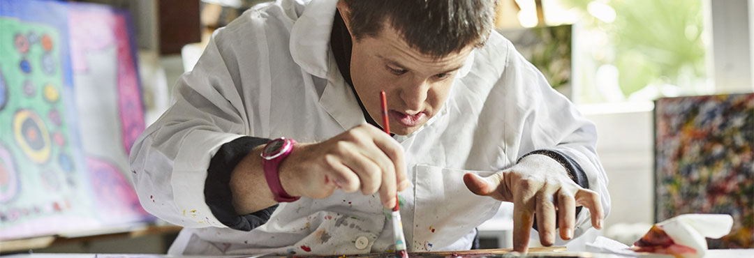 Mid adult man with down syndrome painting on paper in art studio.