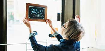 Women hanging an Open sign on a shop front door.