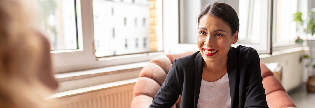 A smiling women sitting on a chair having a conversation.