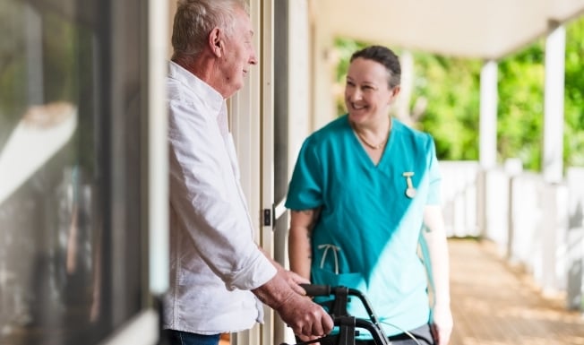 A carer and an elderly male using a walker