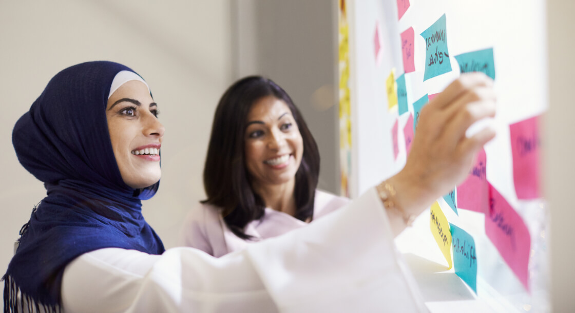 Two women standing in front of a whiteboard sorting colourful post it notes