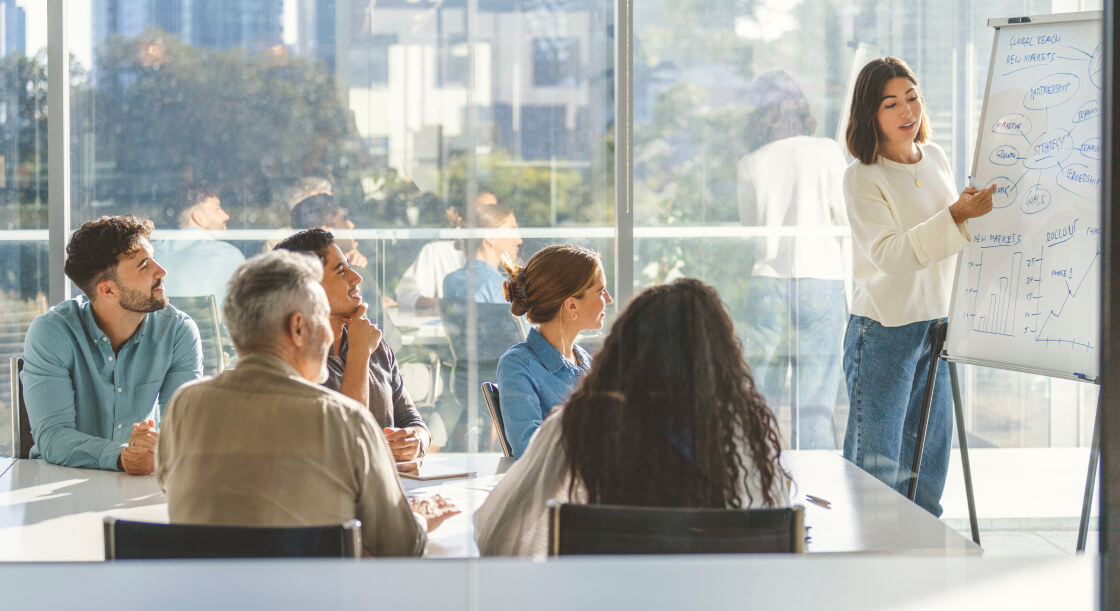 A team of office workers looking at a whiteboard while a woman presents