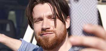 A driver standing beside his car to take a selfie on his mobile phone.