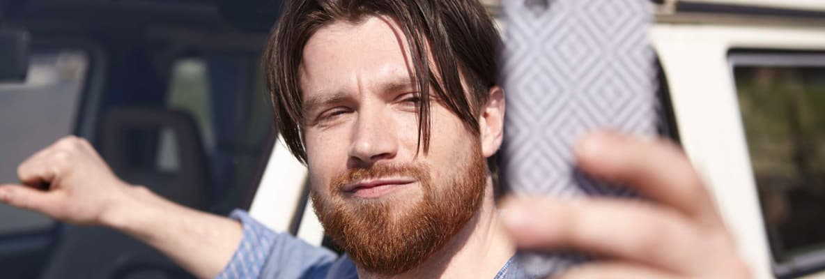 A driver standing beside his car to take a selfie on his mobile phone