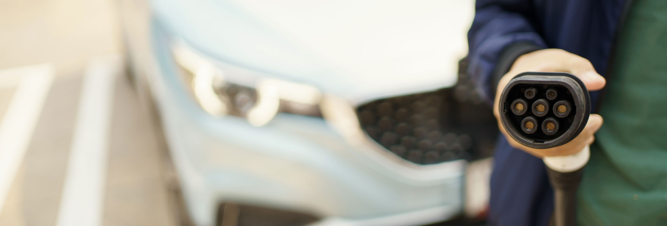 Person standing in front of an electric vehicle holding a charging cable