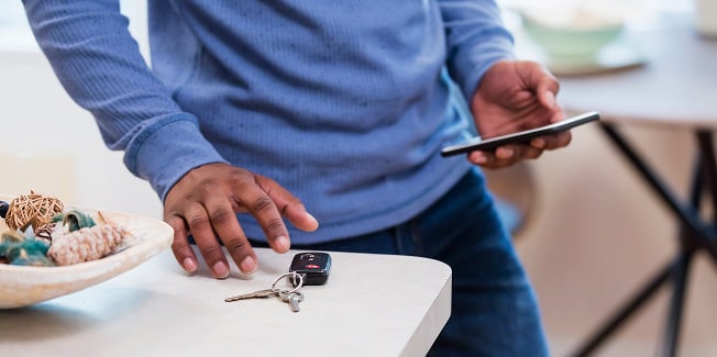 Person placing car keys on a table while holding a smartphone.
