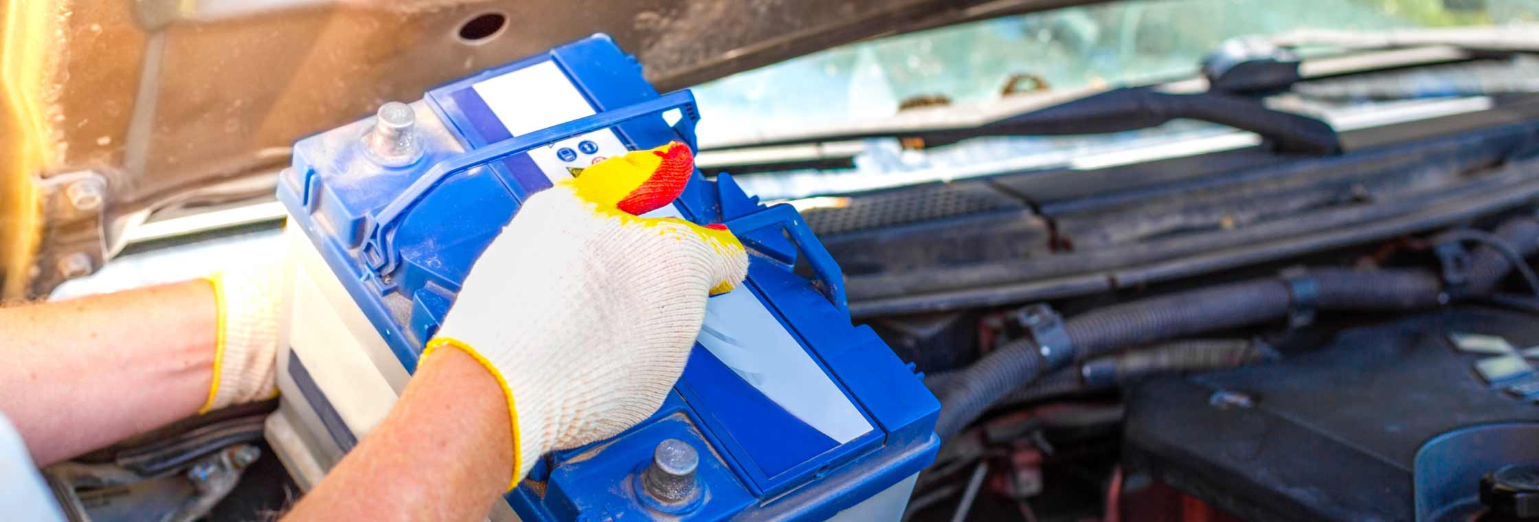 Gloved installer replacing a battery in a vehicle