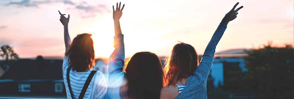 Three people standing with raised arms in front of a sunset.