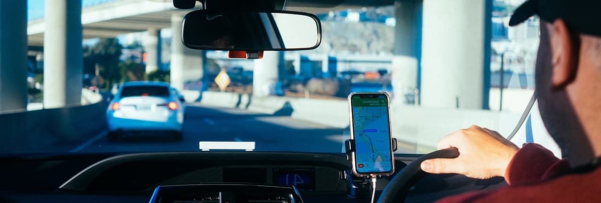 Male driver using mobile phone device secured in a cradle affixed in the car using a navigation mobile application