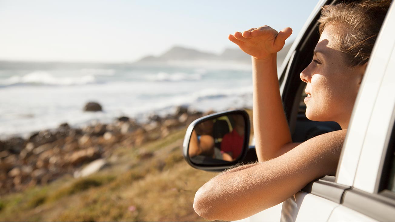 A woman enjoying a coastal view from the window of her safely parked car.