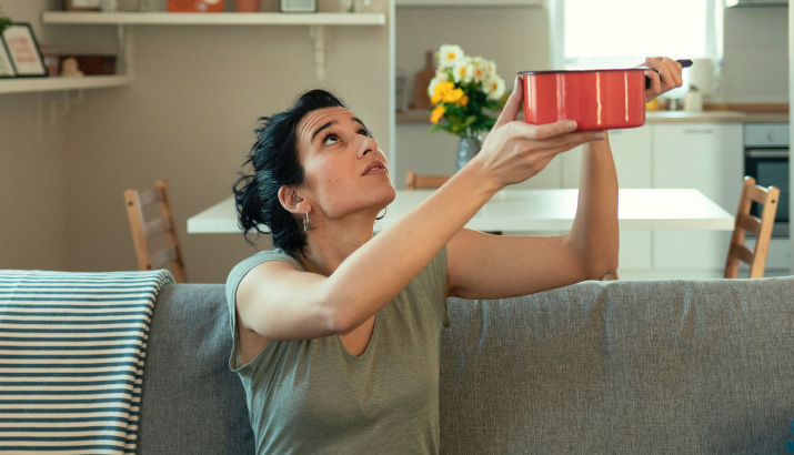 A woman sitting on a sofa holding a saucepan to catch drips.
