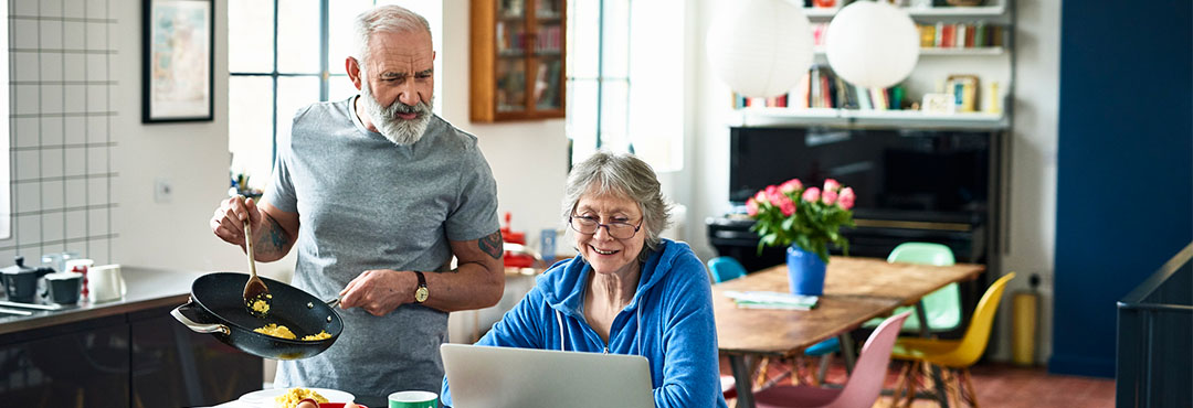 Man with a frypan with eggs and woman reading laptop