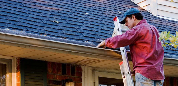 man cleaning leaves out of the roof gutters