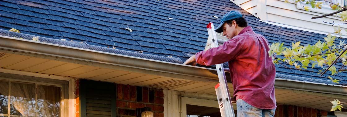 man cleaning leaves out of a roof gutter