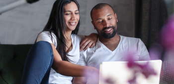 A happy couple sitting on their couch viewing their laptop screen