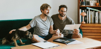 Two men sitting on a sofa reading a document.