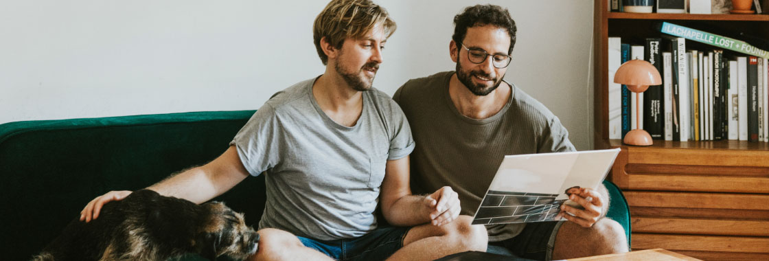 Two men sitting on a sofa reading a brochure together