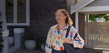 Smiling female departing a residential home and exiting up a driveway with a handbag