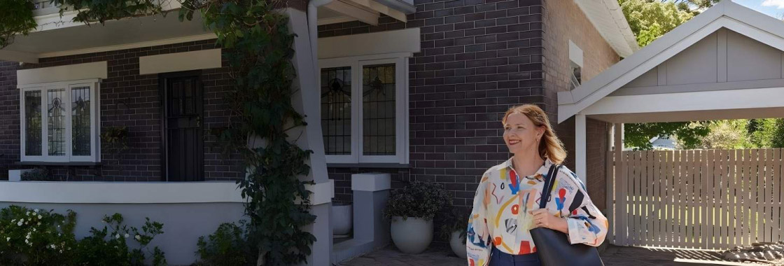 Smiling female departing a residential home and exiting up a driveway with a handbag