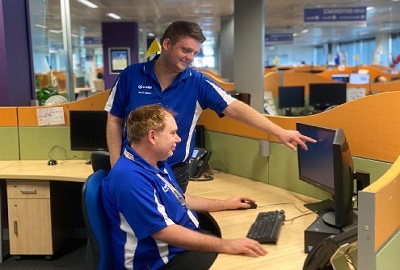 A call centre employee leaning over his colleague and pointing to a computer screen