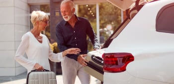 An older couple placing a suitcase in the boot of a car