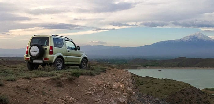 Four wheel drive vehicle at elevation overlooking a mountain scape and a body of water below