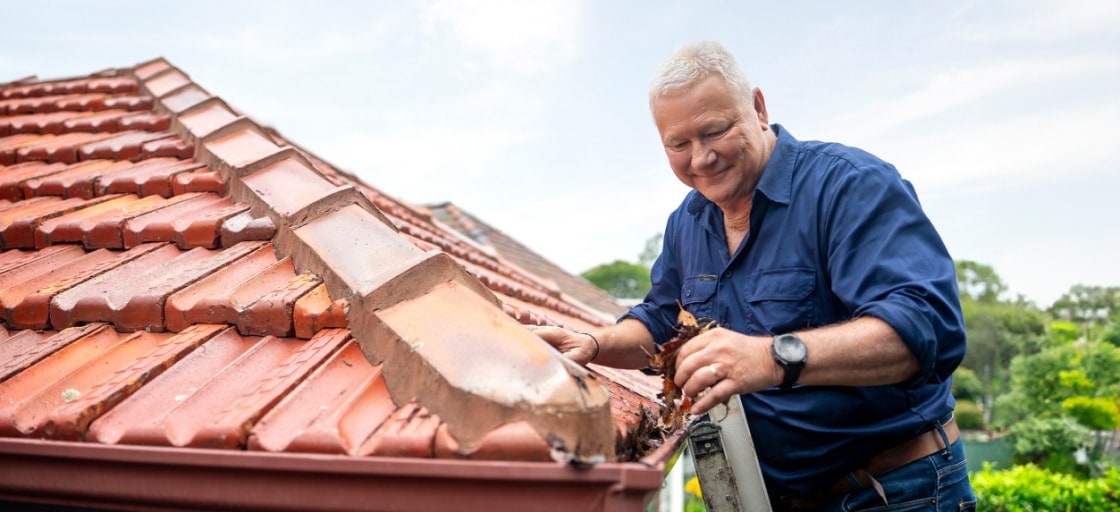Scotty Cam up a ladder clearing leaves out of a roof gutter