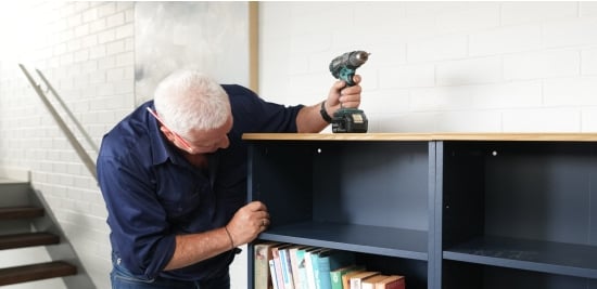 Scotty Cam rests a drill on top of a bookcase as he inspects it