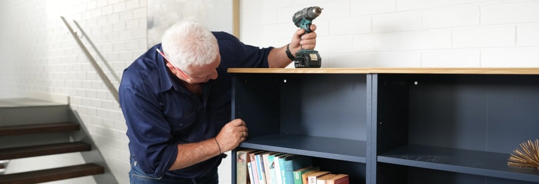 Scotty Cam rests a drill on top of a bookcase as he inspects it