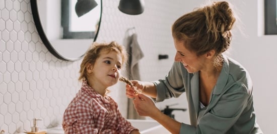 Image of a lady tieing her kid hair in the bathroom