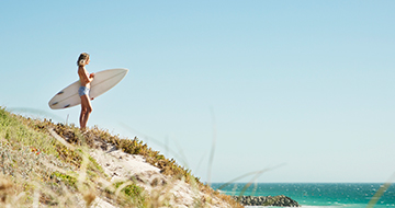 Woman with surfboard looking at the ocean
