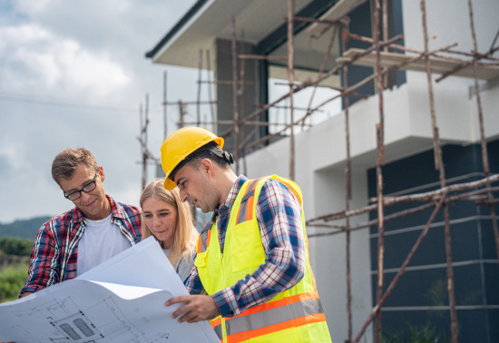 A couple checking floorplans with their builder outside their home.